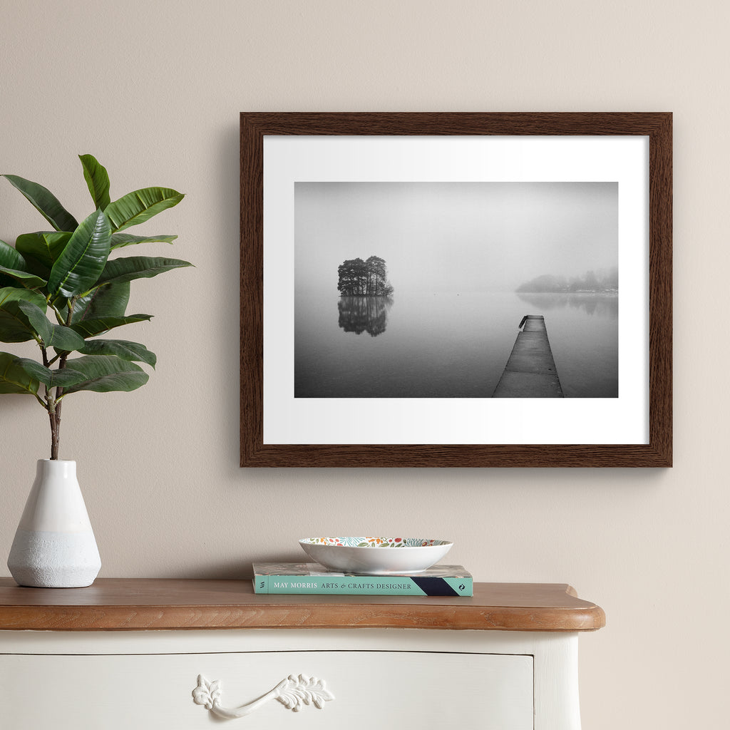Moody black and white photography art print featuring mist flowing over still waters. Art print is hung up on a beige wall.