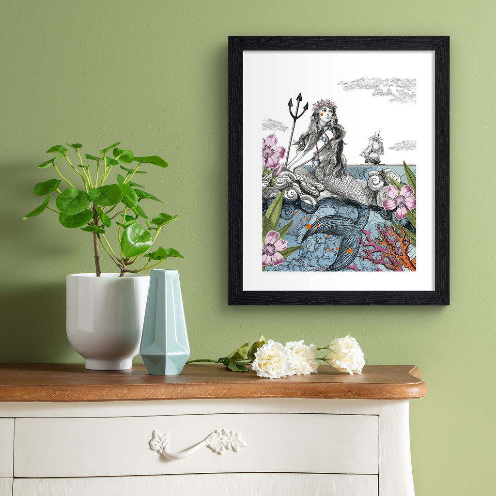 Emotive art print featuring a thoughtful mermaid basking in the shallows, surrounded by nature, with a ship sailing in the background. Art print is hung up on a sage green wall.