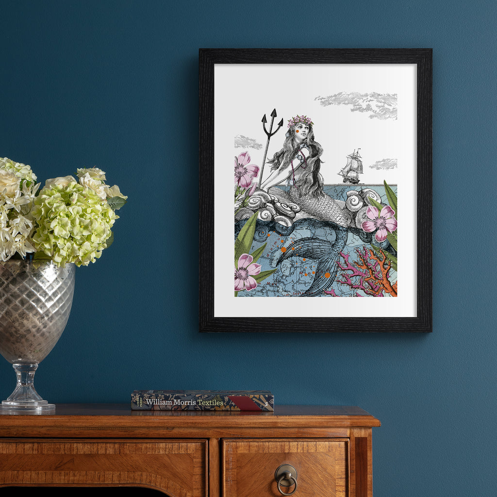 Emotive art print featuring a thoughtful mermaid basking in the shallows, surrounded by nature, with a ship sailing in the background. Art print is hung up on a dark blue wall.