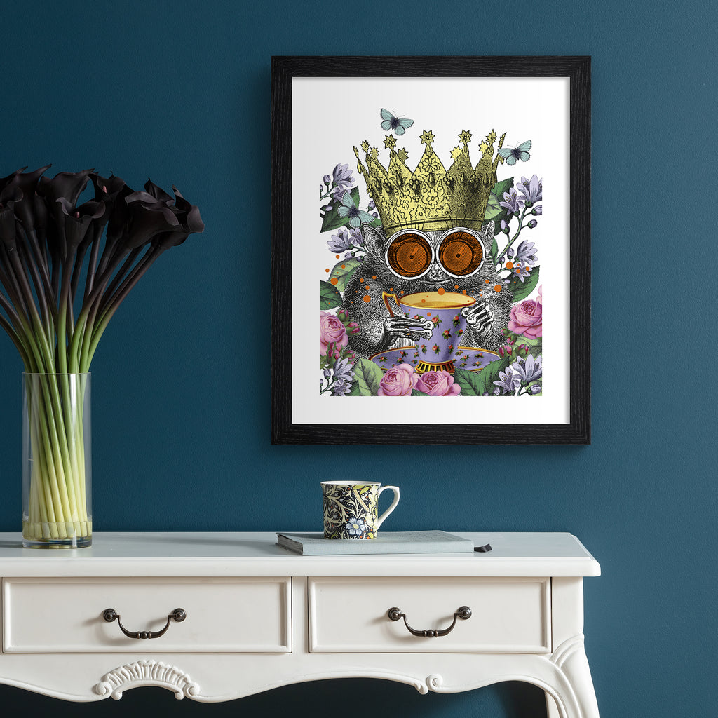 Vibrant illustration art print of a monkey surrounded by botanicals, wearing a crown and holding a cup of tea, hung up on a blue wall.