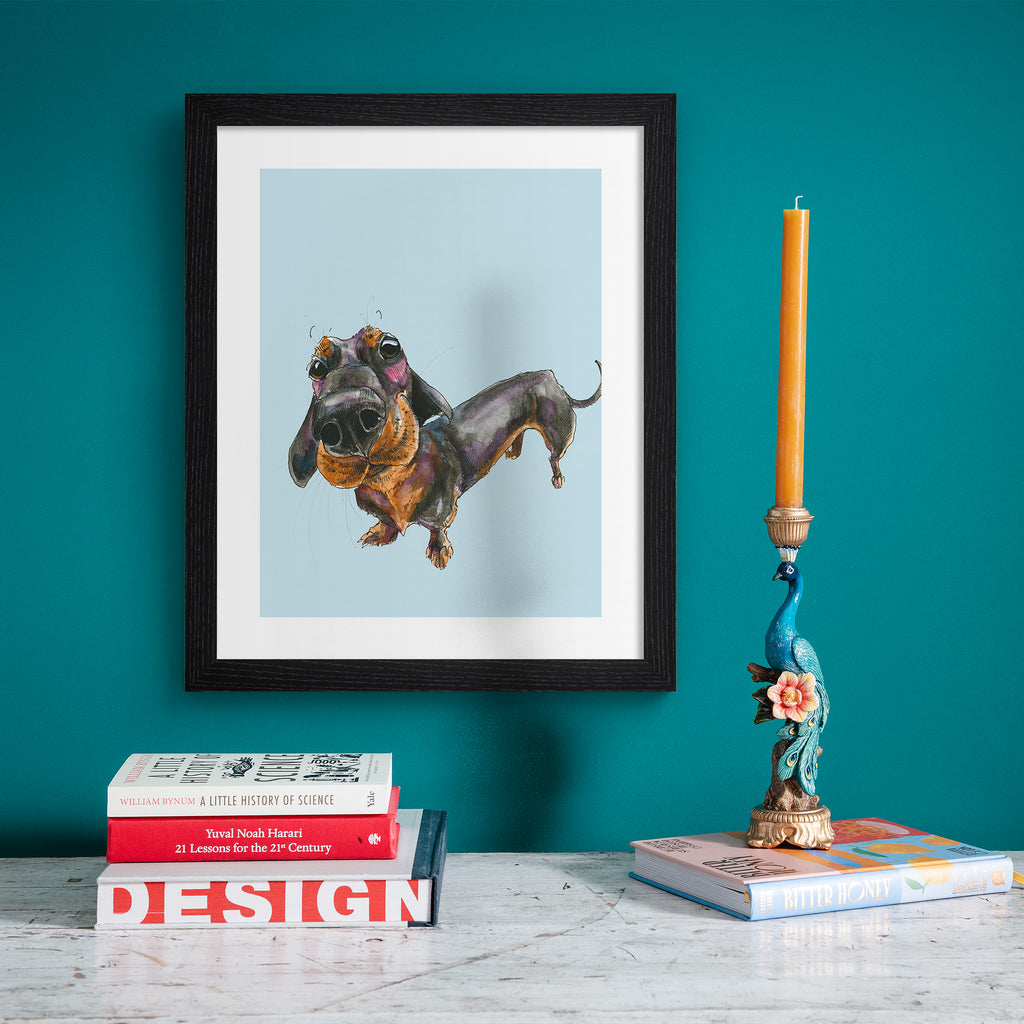 Playful art print featuring a curious dachshund dog, posing in front of a pale blue background. Art print is hung up on a bright blue wall.