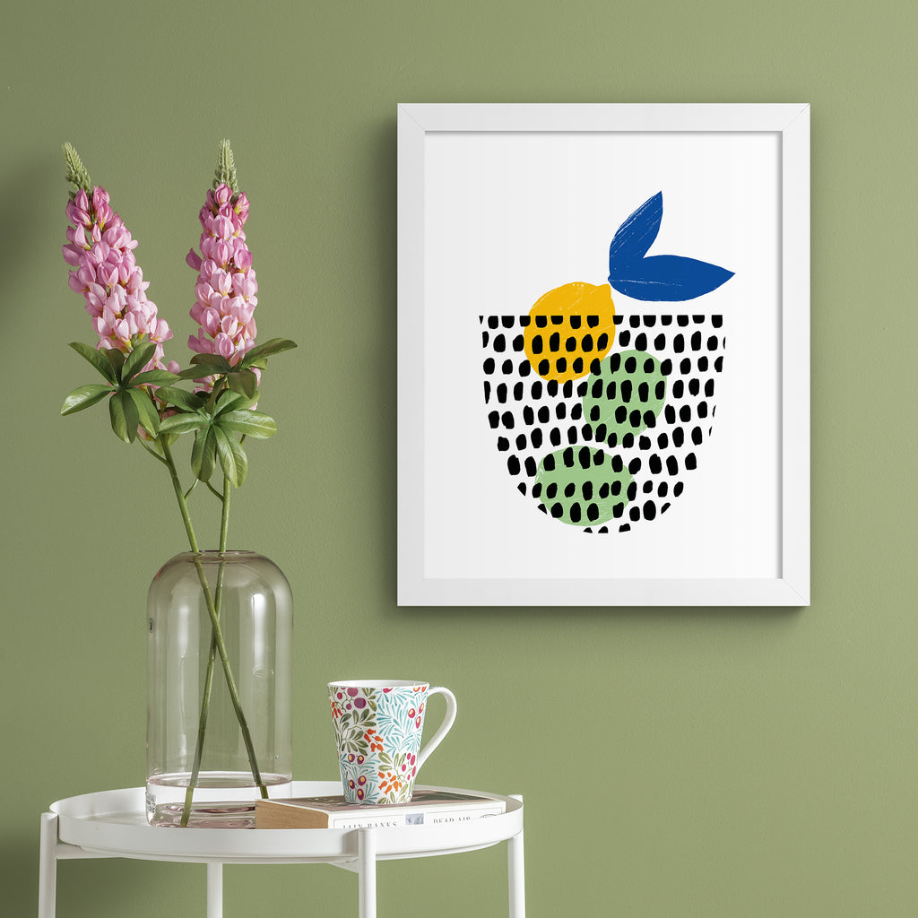 Minimalistic art print featuring a fruit basket containing lemons and limes. Art print is hung up on a sage green wall.