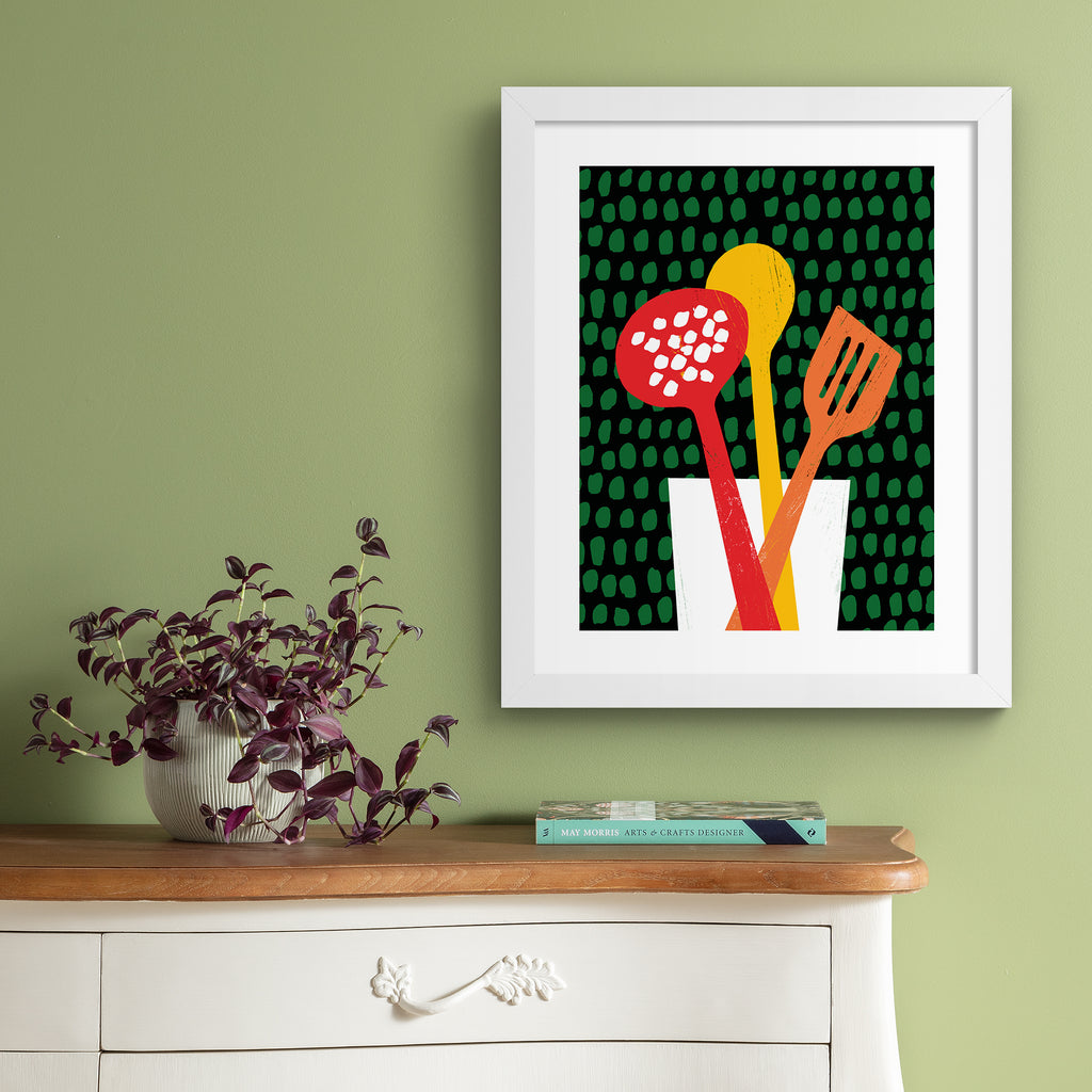 Unique art print featuring brightly coloured utensils in front of a patterned background. Art print is hung up on a green wall.