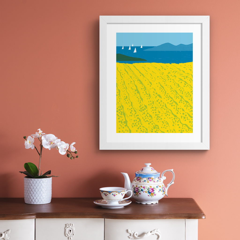 Minimalistic art print featuring beautiful yellow fields bordered by a coastal view.  Art print is hung up on a pink wall.
