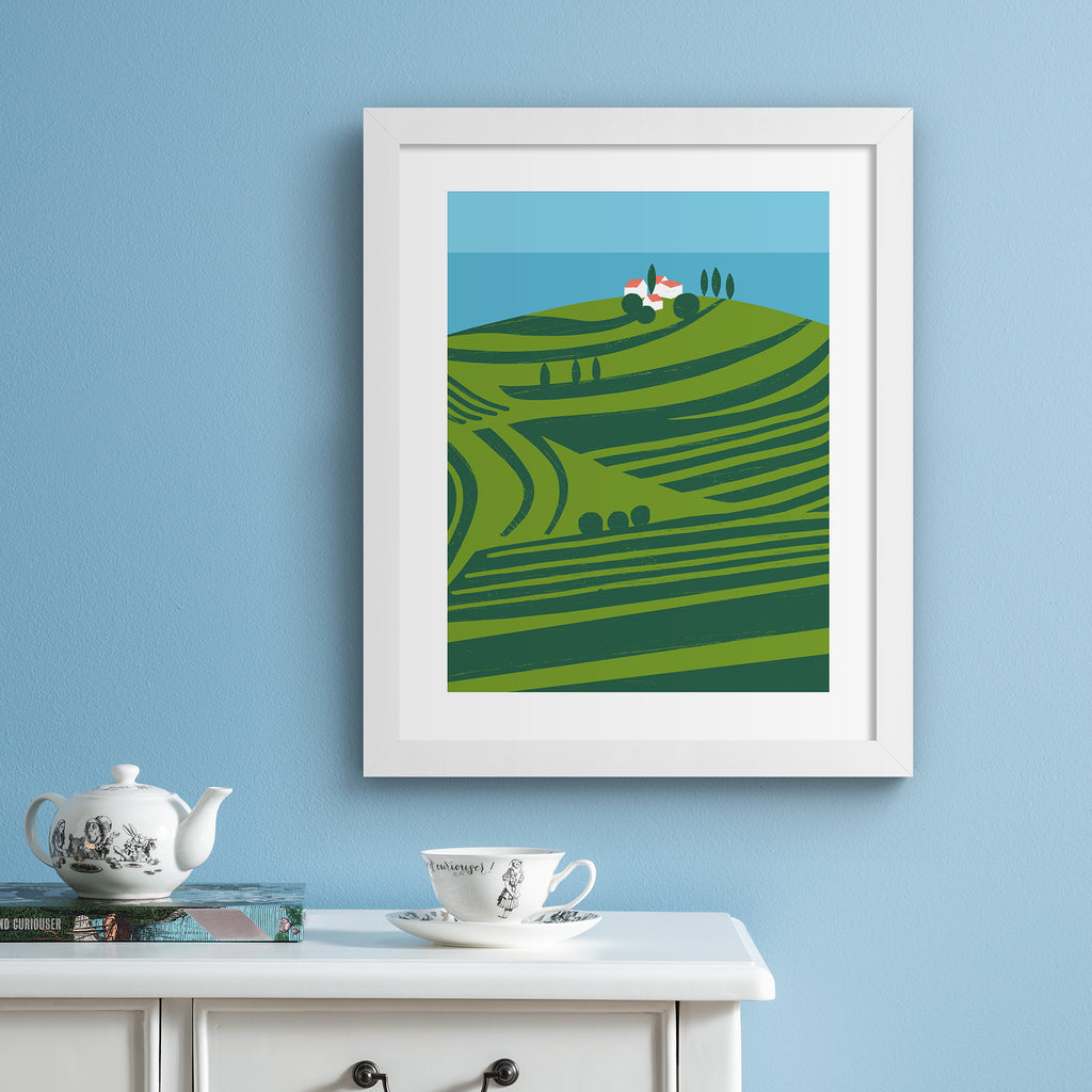Vivid art print containing a sweeping scene of vineyards on the coast. Art print is hung up on a blue wall.