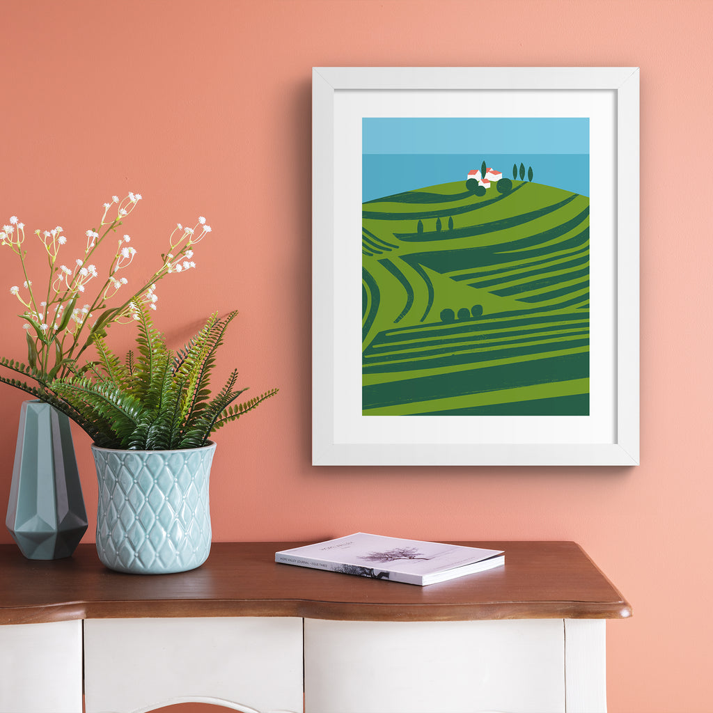 Vivid art print containing a sweeping scene of vineyards on the coast. Art print is hung up on a pink wall.