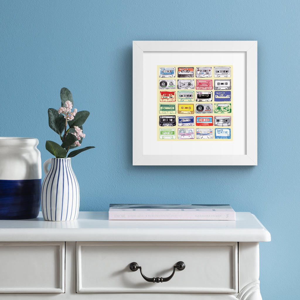 Bright art print featuring different types of mix tapes on a yellow background. Art print is hung up on a light blue wall.