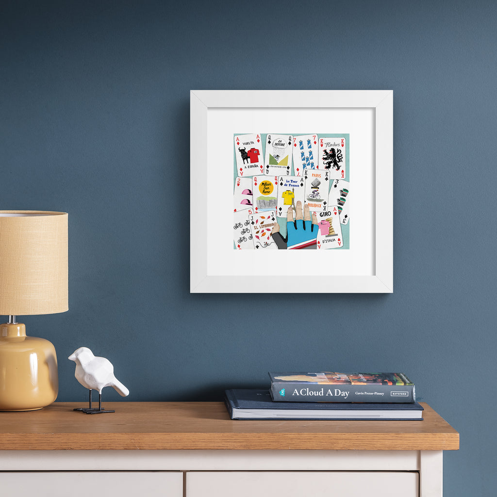 Art print featuring a deck of cards splayed out on a table. Art print is hung up on a dark blue wall.