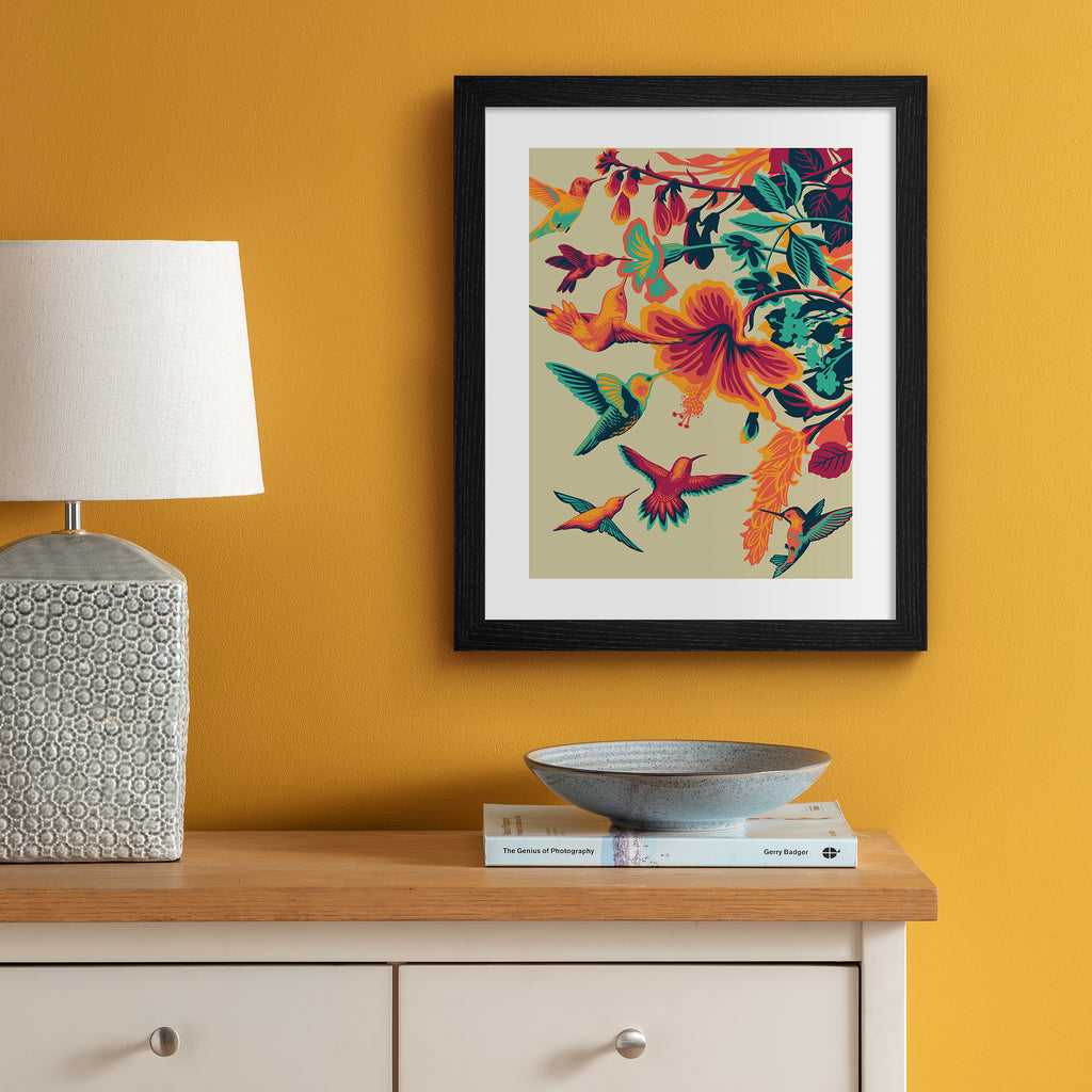 Striking art print featuring brightly coloured hummingbirds hovering above vibrant flowers. Art print is hung up on an orange wall.