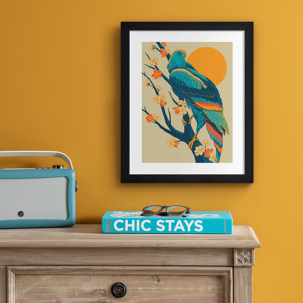 Colourful print featuring a detailed illustration of a peregrine falcon perched in front of a brilliant sunrise. Art print is hung up on an orange wall.