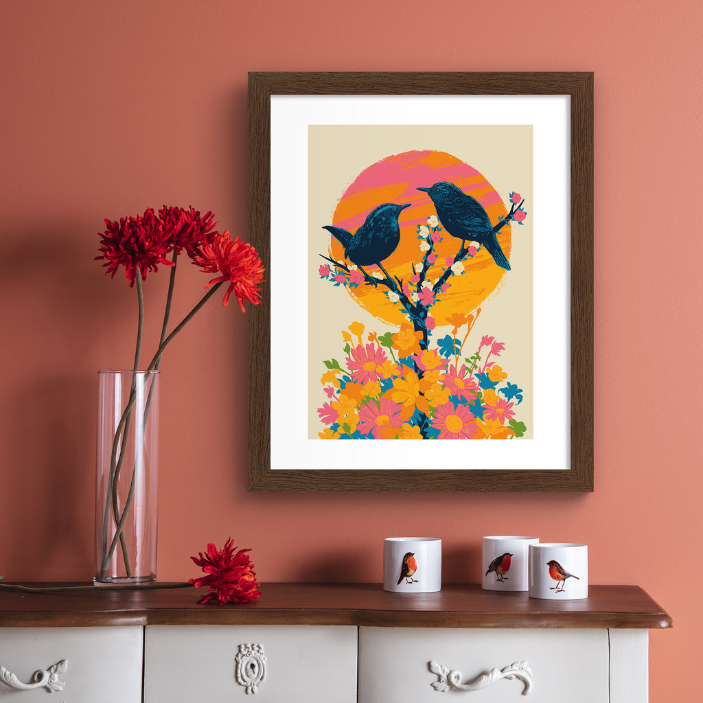 Brilliant art print featuring a detailed illustration of two birds perching on a blooming tree, in front of a bright sunset. Art print is hung up on a pink wall.