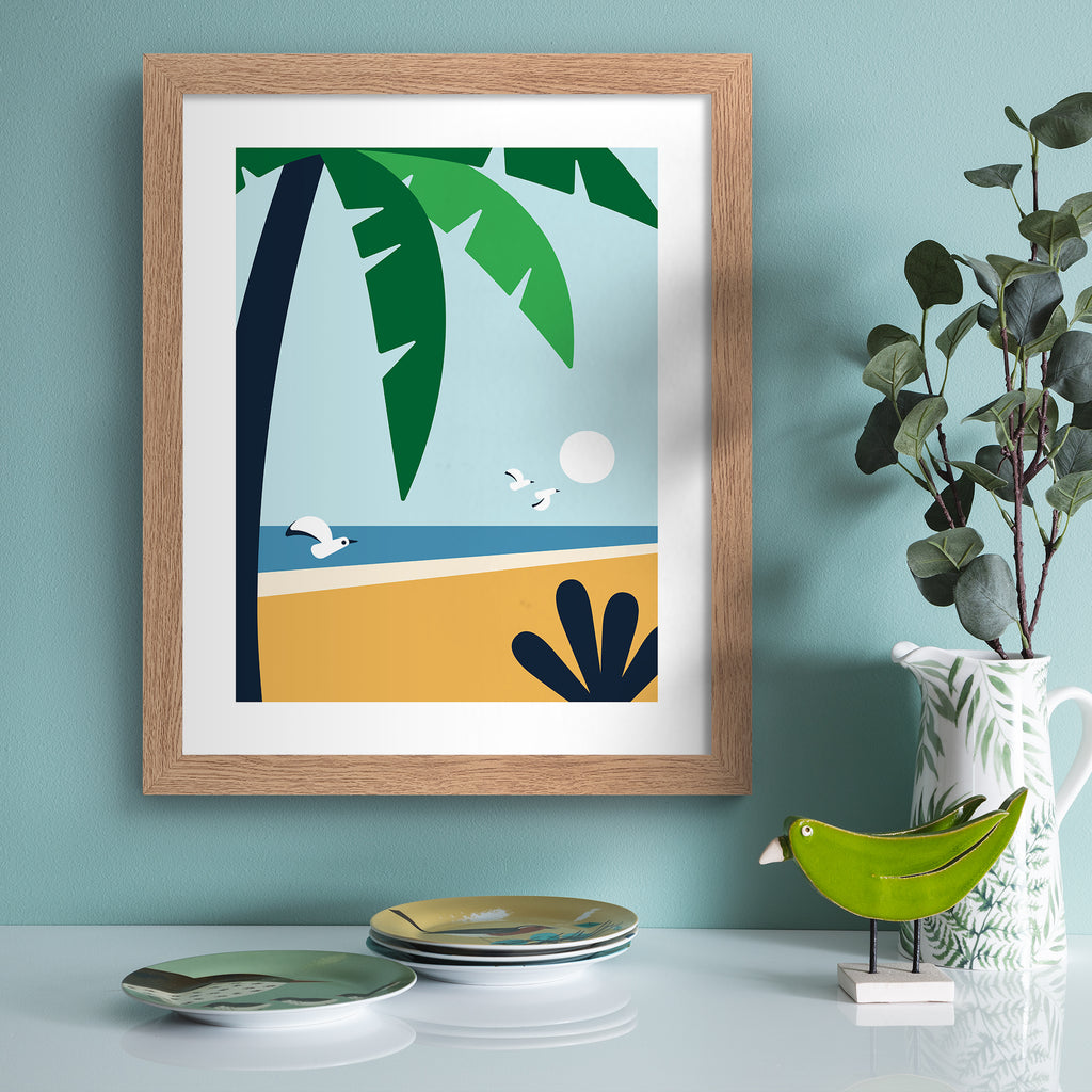 Minimalistic print featuring a palm tree standing in front of a beautiful coastal scene. Art print is hung up on a light blue wall.