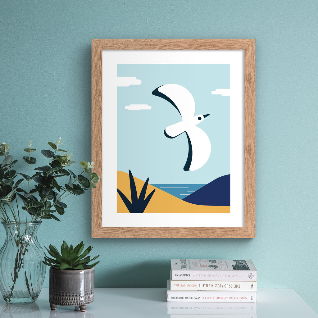 Colourful art print featuring a bird flying in front of a coastal scene. Art print is hung up on a pale blue wall.