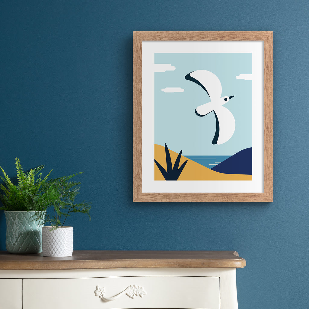 Colourful art print featuring a bird flying in front of a coastal scene. Art print is hung up on a dark blue wall.