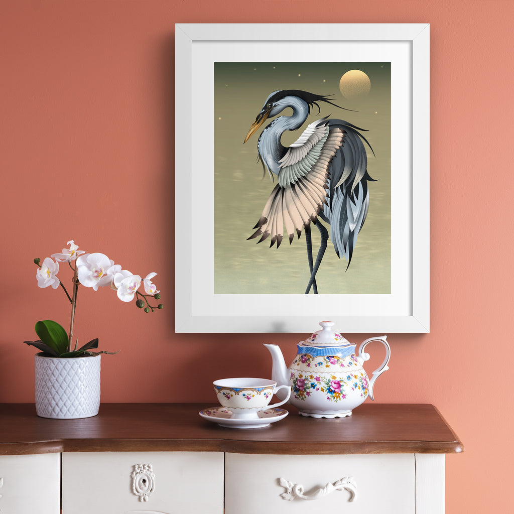 Moody art print featuring a heron basking in front of a golden sun. Art print is hung up on a coral wall.