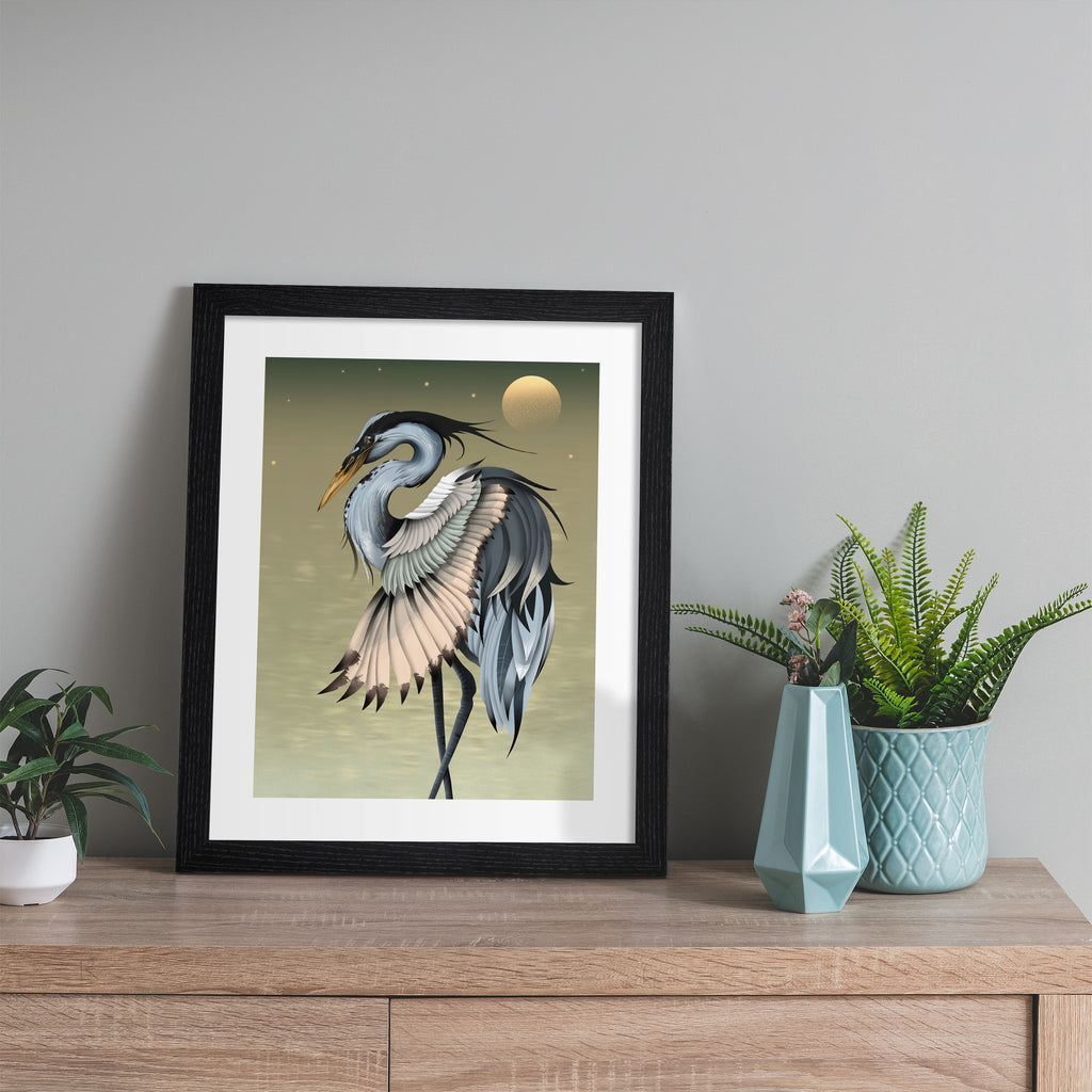 Moody art print featuring a heron basking in front of a golden sun. Art print is leaning against a grey wall.
