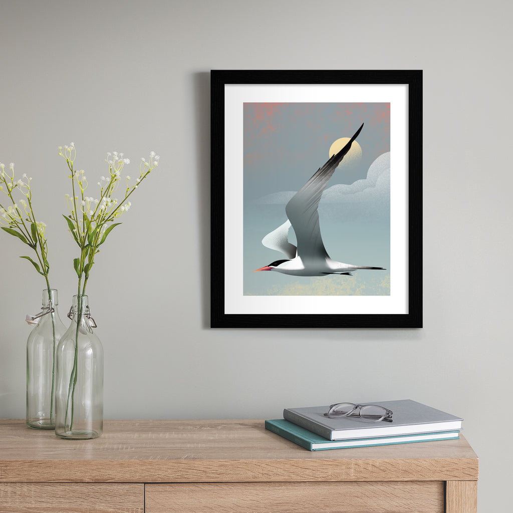 Striking art print featuring a grey tern flying in front of a moody blue sky. Art print is hung up on a blue wall.