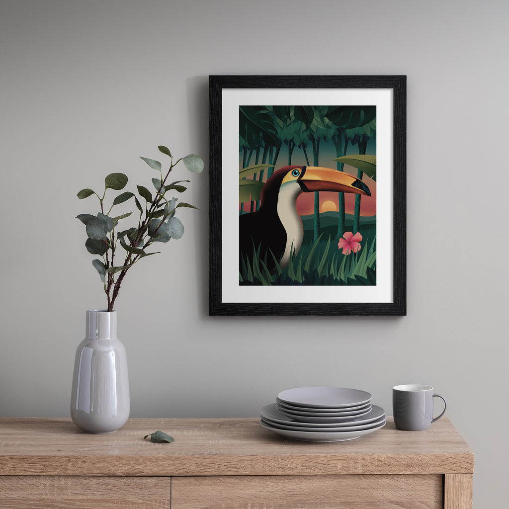 Vibrant art print featuring a sunset forest scene of a toucan standing amidst the trees. Art print is hung up on a grey frame.
