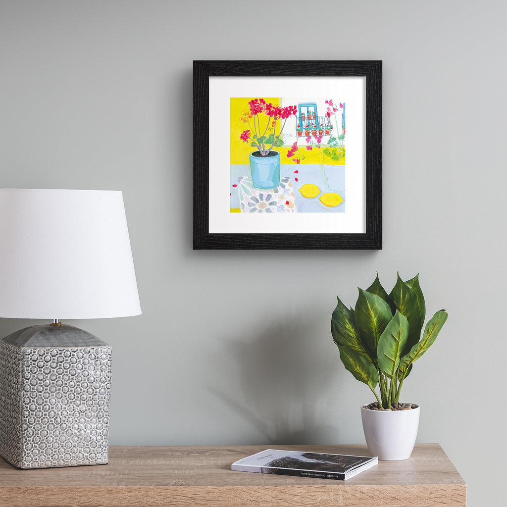 Vibrant art print featuring a vase of pink flowers next to yellow fruit and walls. Art print is hung up on a silvery wall.