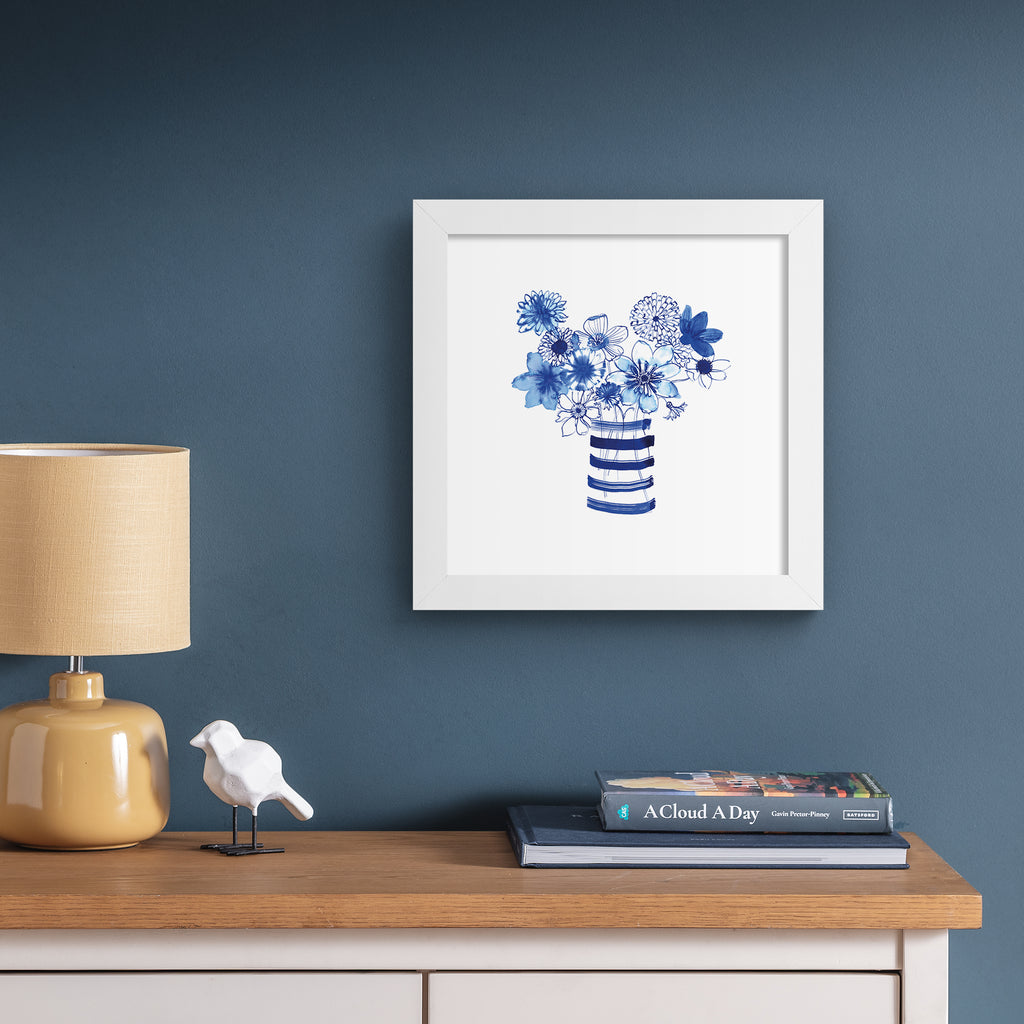 Colourful art print featuring indigo blue flowers in a striped vase. Art print is hung up on a dark blue wall.
