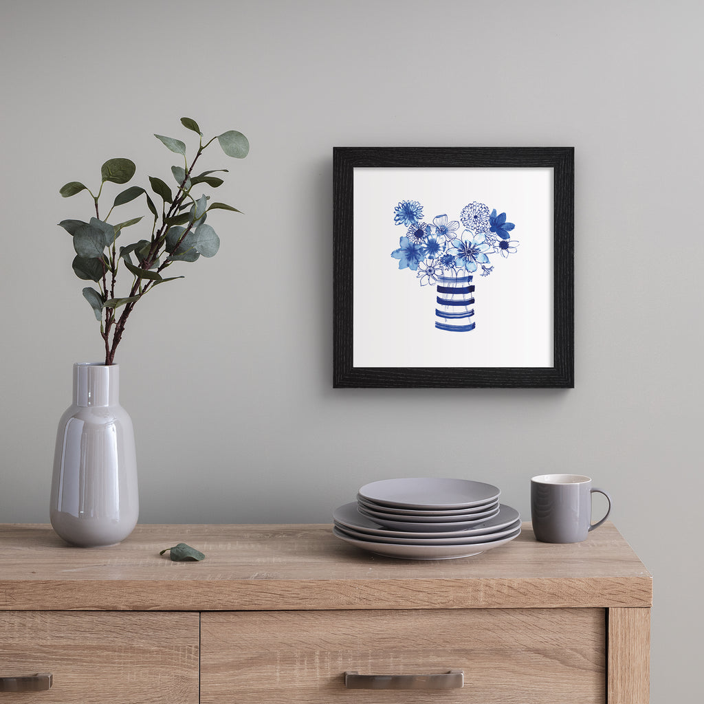 Colourful art print featuring indigo blue flowers in a striped vase.  Art print is hung up on a silver wall.