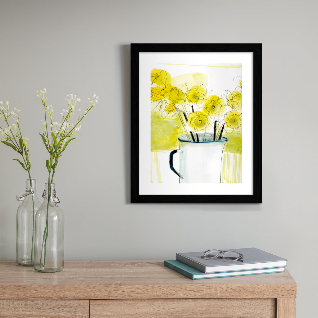 Beautiful yellow art print illustration featuring daffodils spilling out of an enamel jug, with a blended yellow and white background. Art print is hung up on a grey wall.
