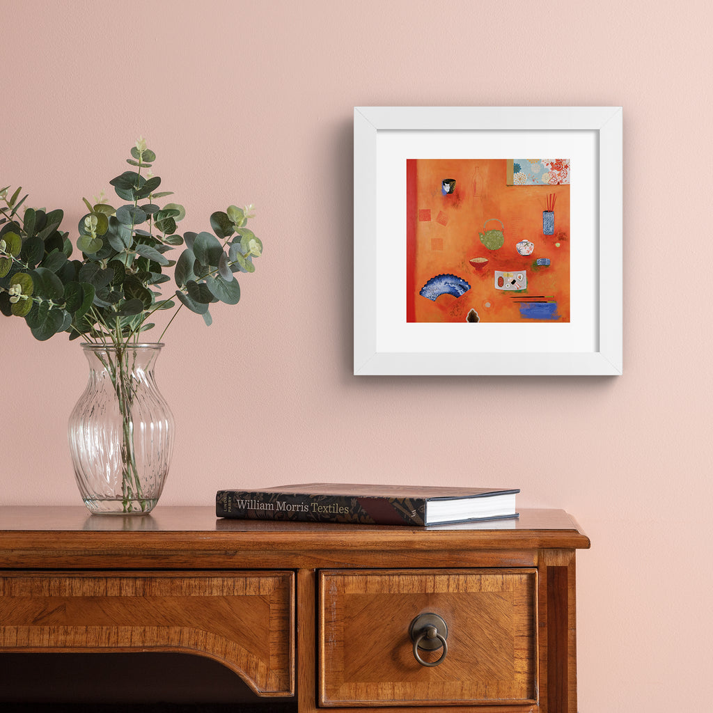 Bright art print featuring different household objects placed on a bright orange background. Art print is hung up on a pale pink wall.