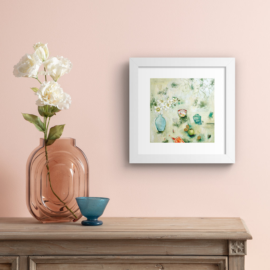 Abstract art print containing an assortment of food and household objects, laid out on a pale green background. Art print is hung up on a pale pink wall.