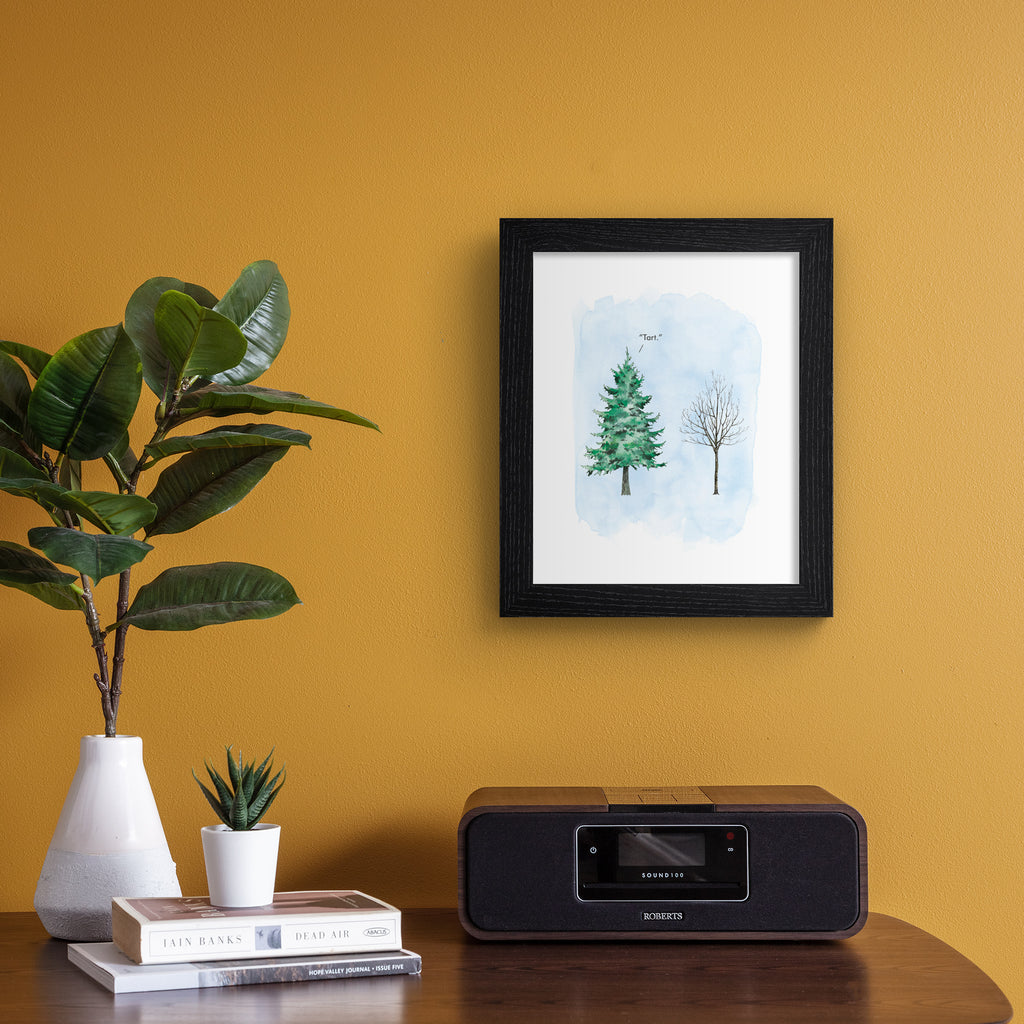 Humorous art print featuring an illustration of a flourishing tree next to a wintery tree with no leaves. Title above tree reads 'Tart'. Art print is hung up on an orange wall.