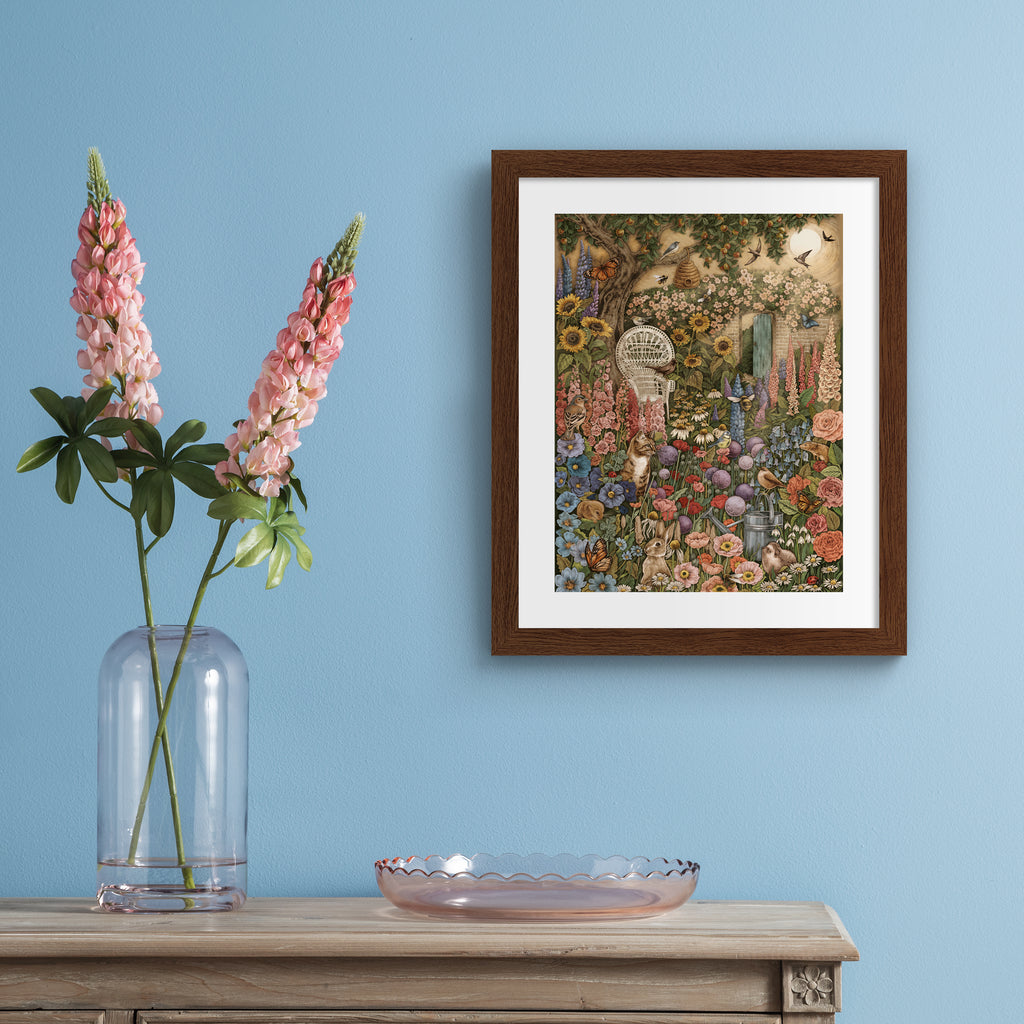 Art print featuring a collection of British wildlife and Summer botanicals in an atmospheric nature scene. A cat sits amongst the flowers, with a garden chair nearby. Art print is hung up on a blue wall.