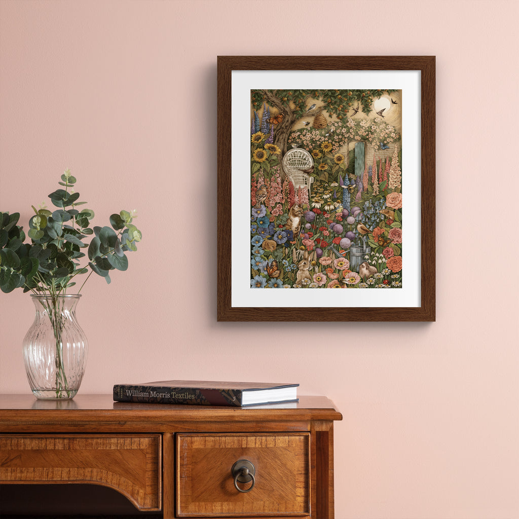 Art print featuring a collection of British wildlife and Summer botanicals in an atmospheric nature scene. A cat sits amongst the flowers, with a garden chair nearby. Art print is hung up on a pink wall.