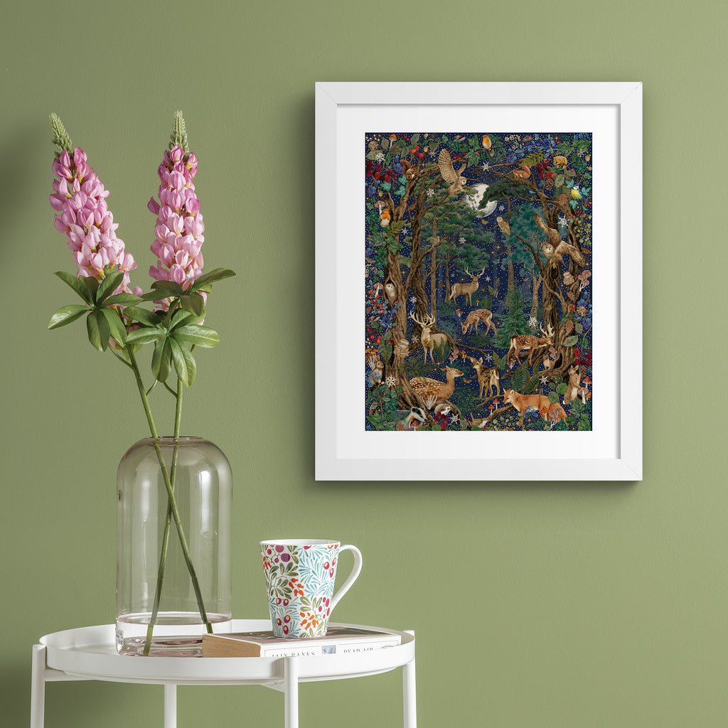 Stunning Christmas art print featuring a collection of British wildlife and botanicals in a forest under a star-studded night sky. Art print is hung up on a green wall.