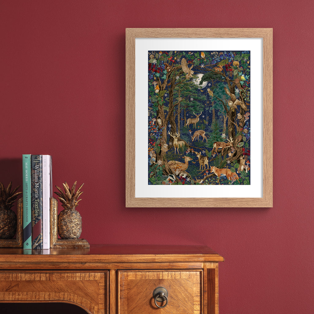 Stunning Christmas art print featuring a collection of British wildlife and botanicals in a forest under a star-studded night sky. Art print is hung up on on a red wall.