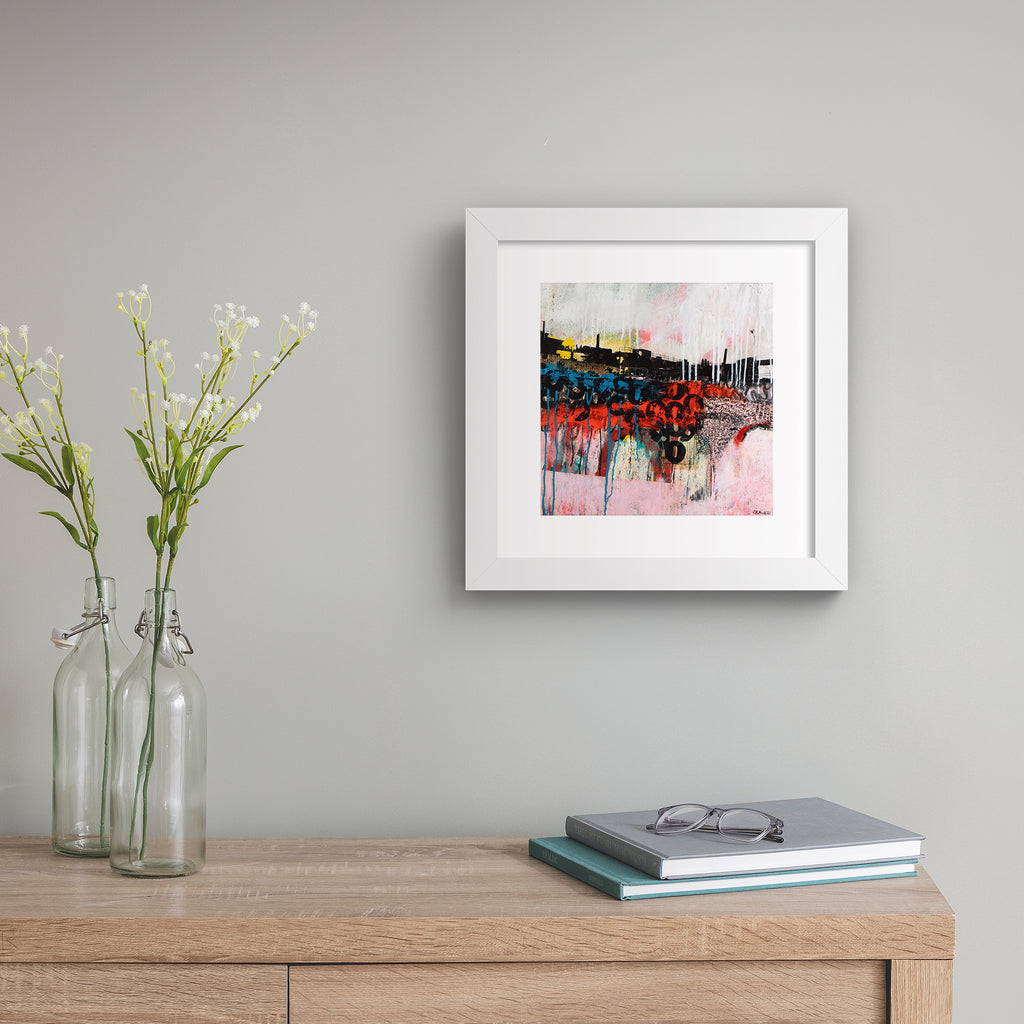 Abstract art print featuring an urban landscape against a brightly coloured background and black graffiti letters. Art print is hung up on a beige wall.