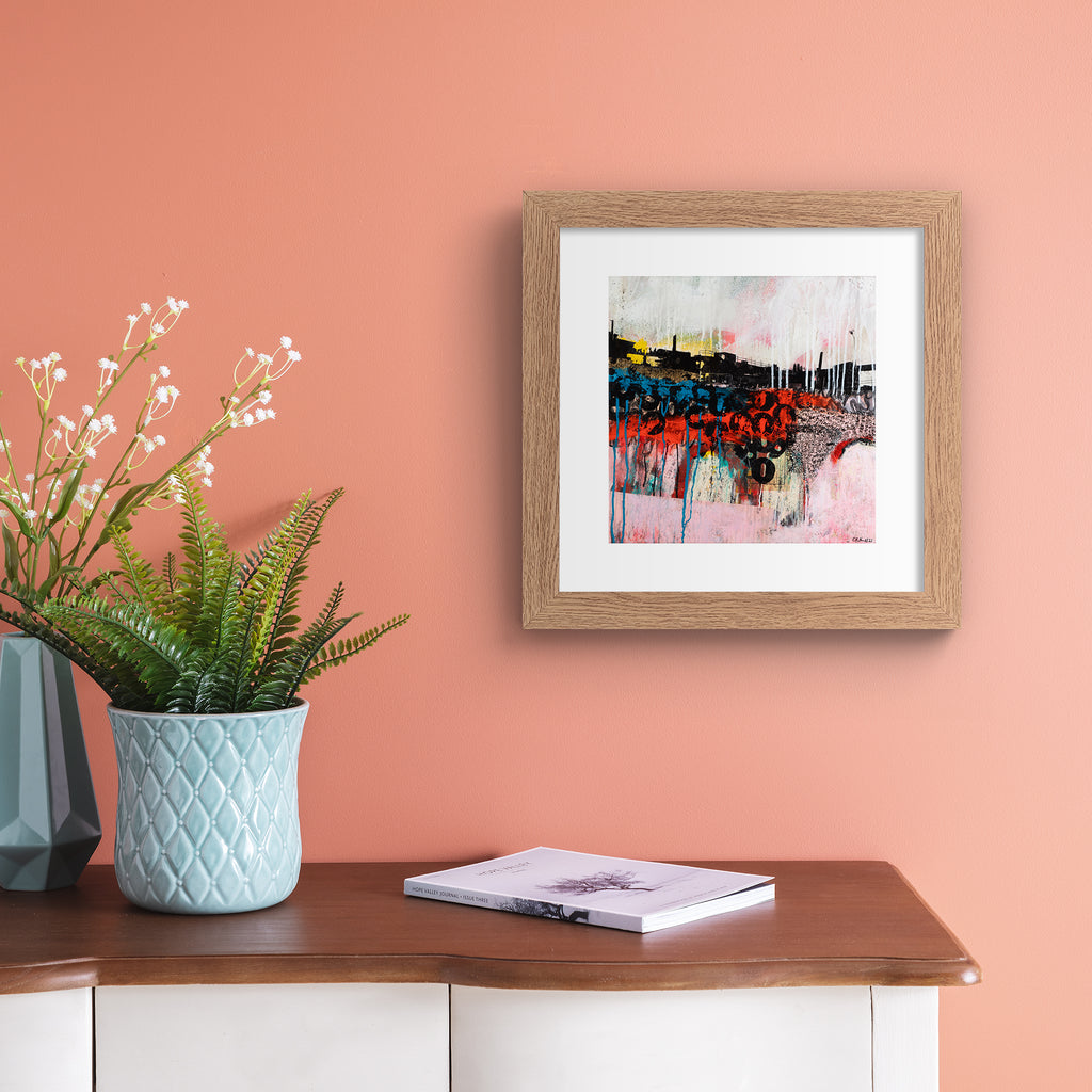 Abstract art print featuring an urban landscape against a brightly coloured background and black graffiti letters. Art print is hung up on a coral wall.