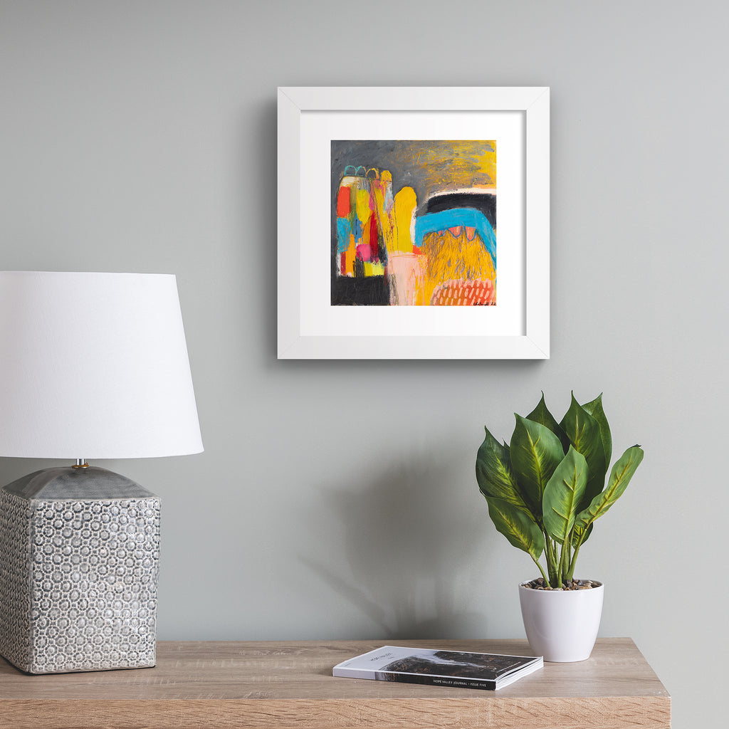 Vivid abstract print featuring an urban array of mixed colours on a dark background. Art print is hung up on a grey wall.