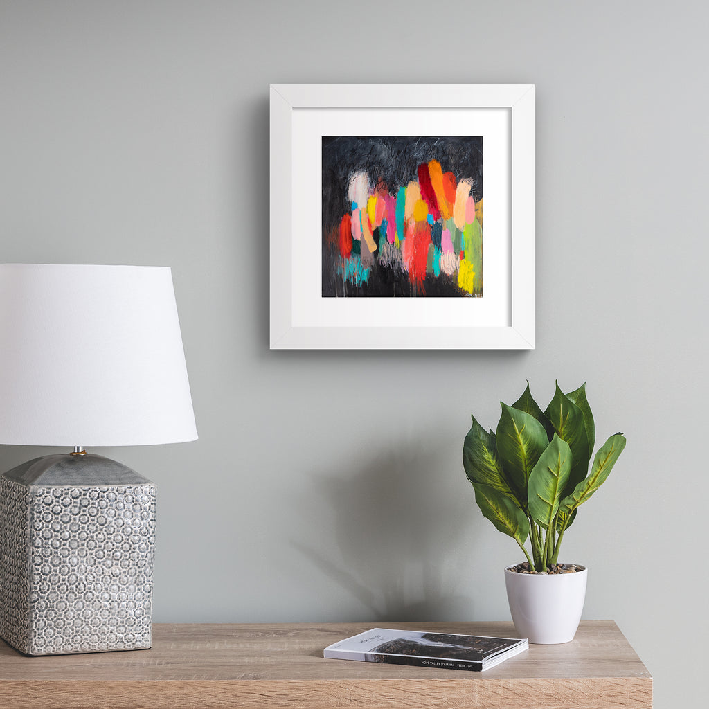 Vivid abstract print featuring a vast array of colours blended together on a moody background. Art print is hung up on a blue wall.