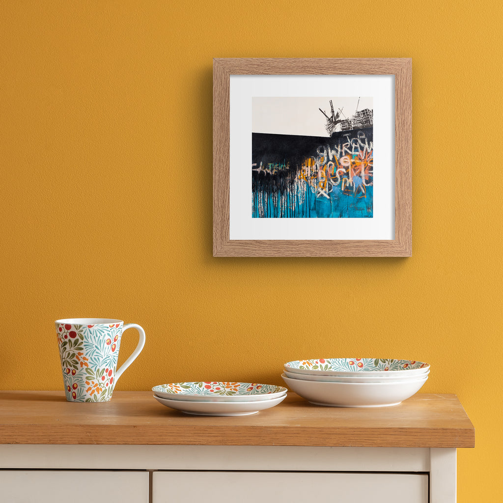 Vivid abstract print featuring an urban landscape covered in black, blue, white and orange graffiti. Art print is hung up on an orange wall.