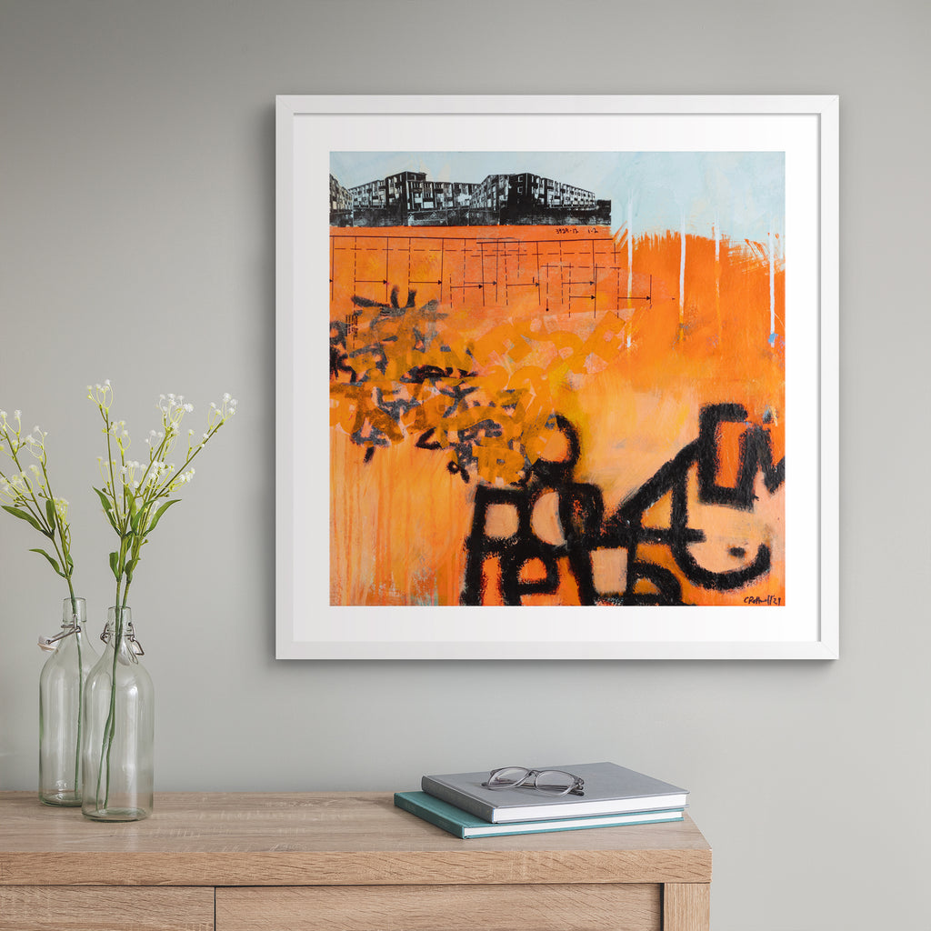Large vivid abstract print featuring an urban landscape covered in bright orange and black graffiti spray paint.  Art print is hung up on a grey wall.