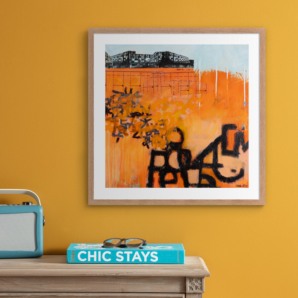 Large vivid abstract print featuring an urban landscape covered in bright orange and black graffiti spray paint. Art print is hung up on an orange wall.