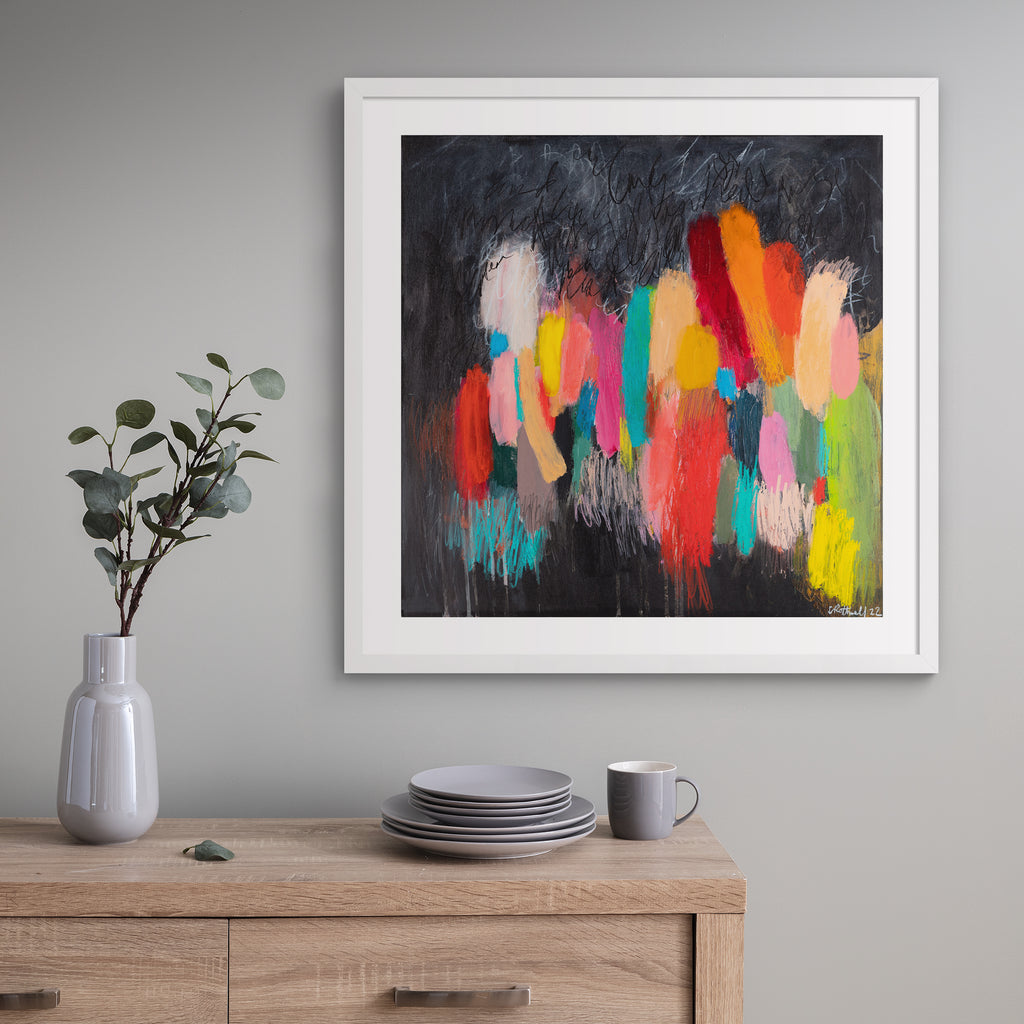 Large version of the vivid abstract print features a vast array of bright colours blended on a moody background. Art print is hung up on a grey wall.