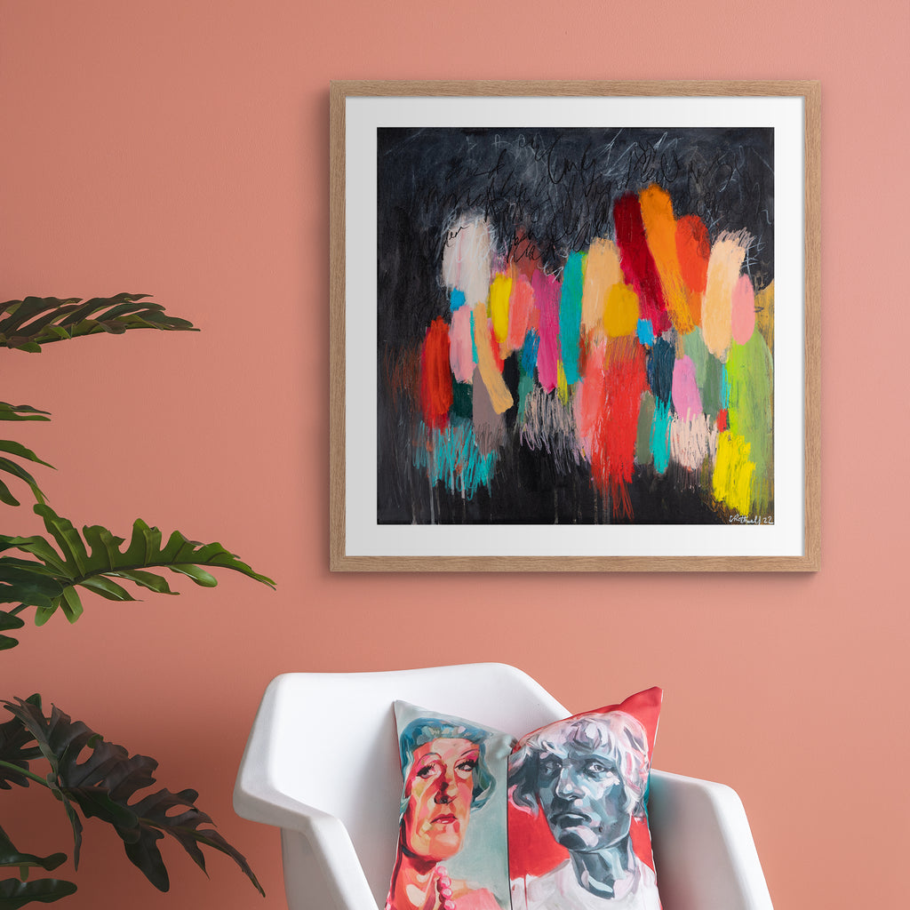 Large version of the vivid abstract print features a vast array of bright colours blended on a moody background. Art print is hung up on a pink wall.