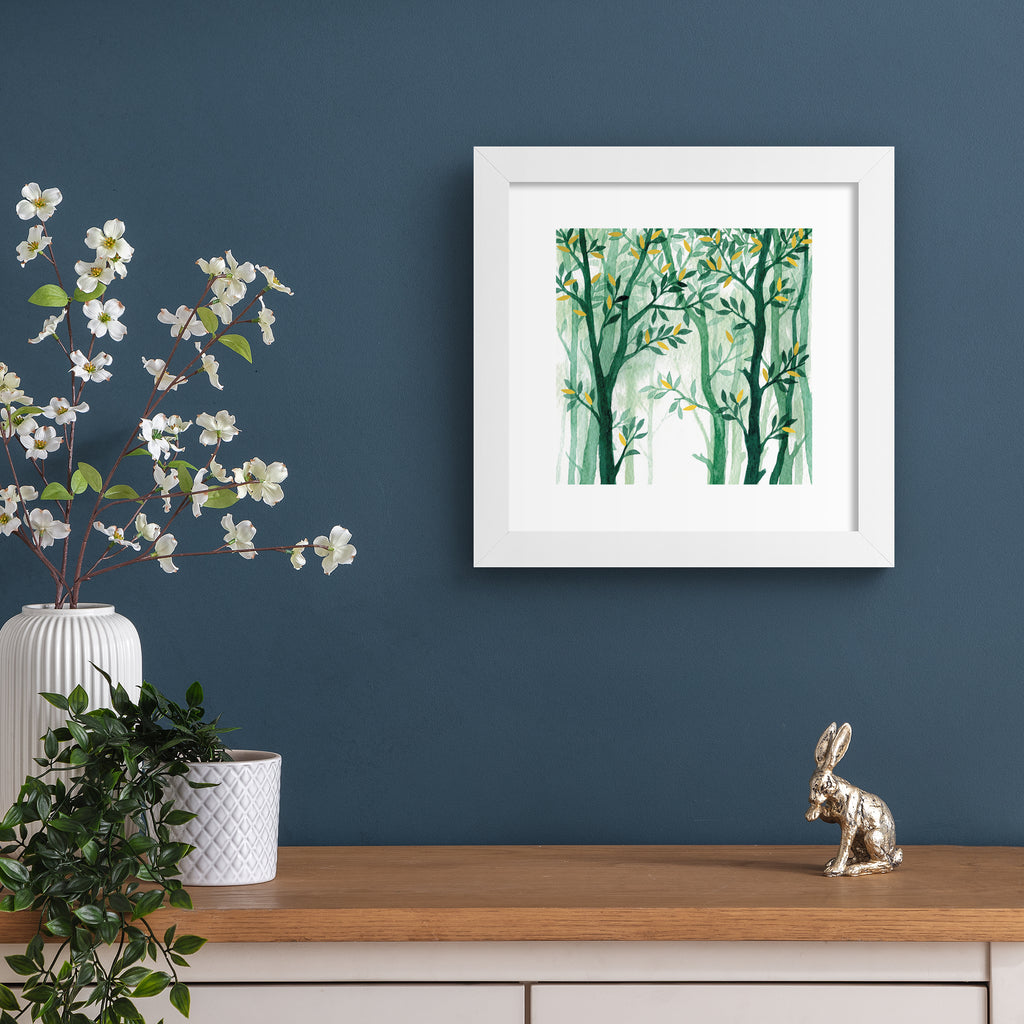 Nature wall art print featuring a forest of vibrant green trees with gold leaves, hung up on a dark blue wall.