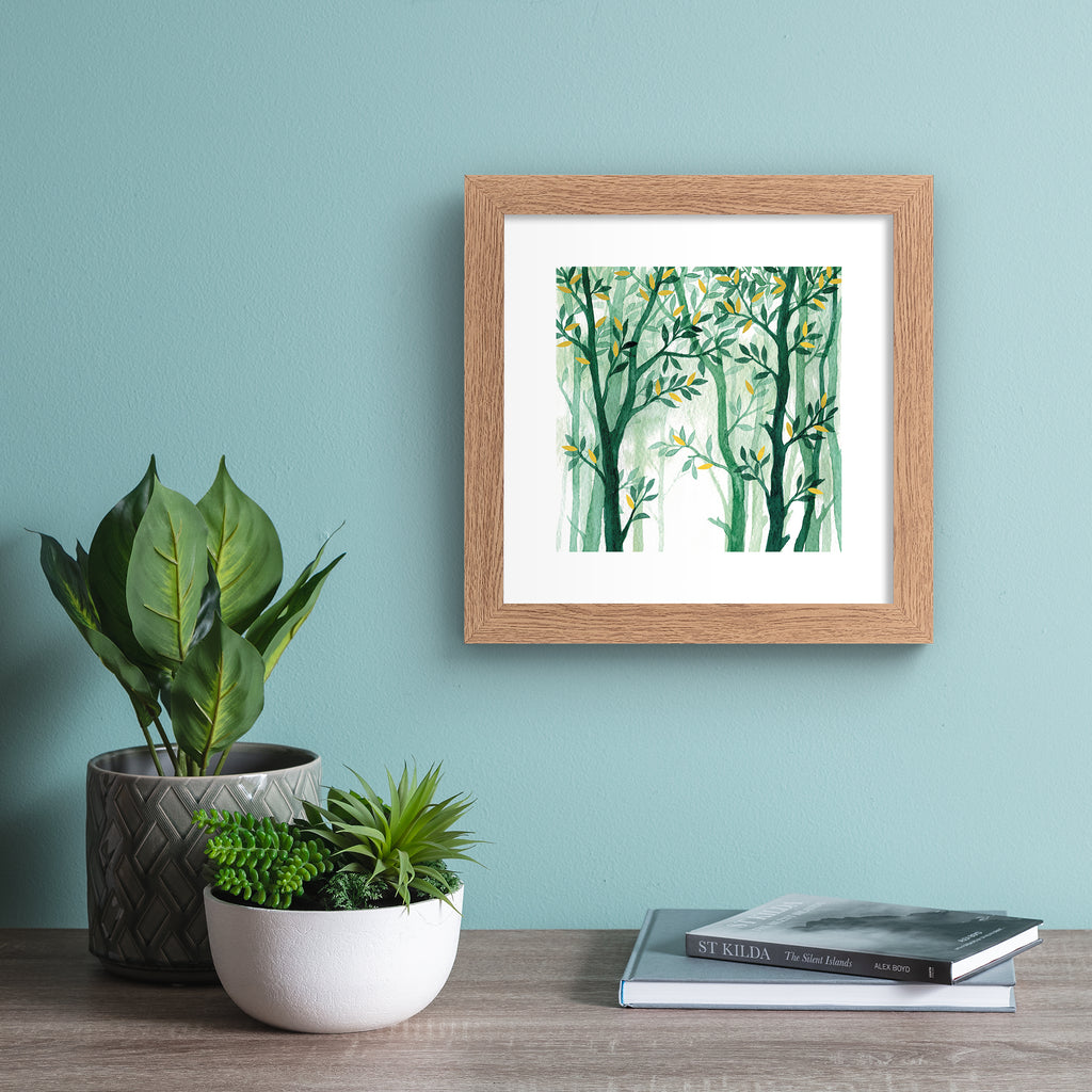 Nature wall art print featuring a forest of vibrant green trees with gold leaves, hung up on a bright blue wall.
