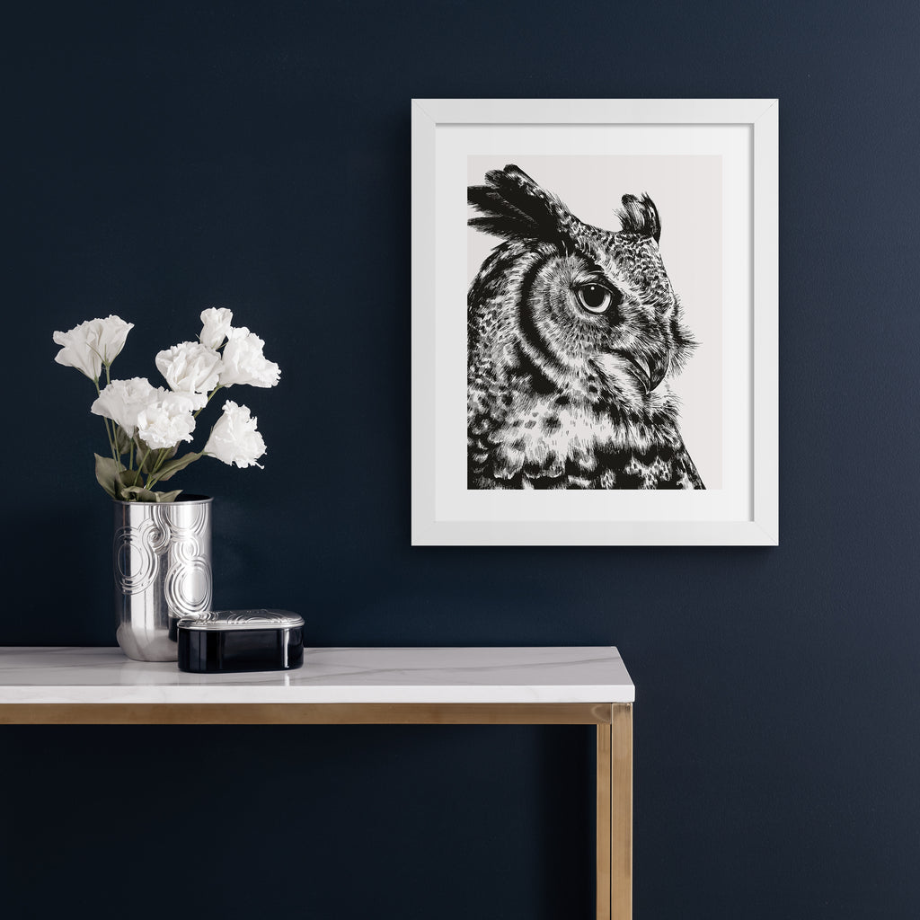 Striking art print featuring a detailed illustration of a great horned owl, in black and white. Art print is hung up on a blue wall.