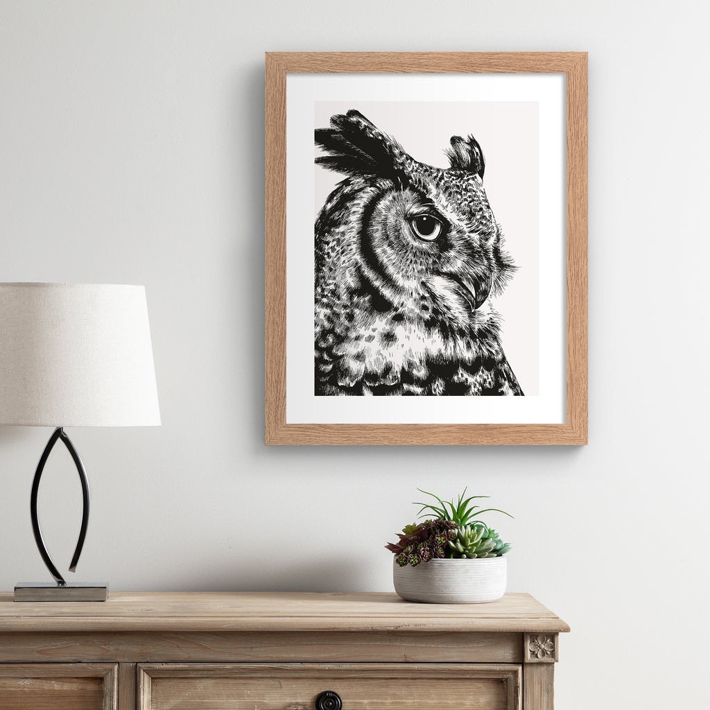 Striking art print featuring a detailed illustration of a great horned owl, in black and white. Art print is hung up on a w white wall.