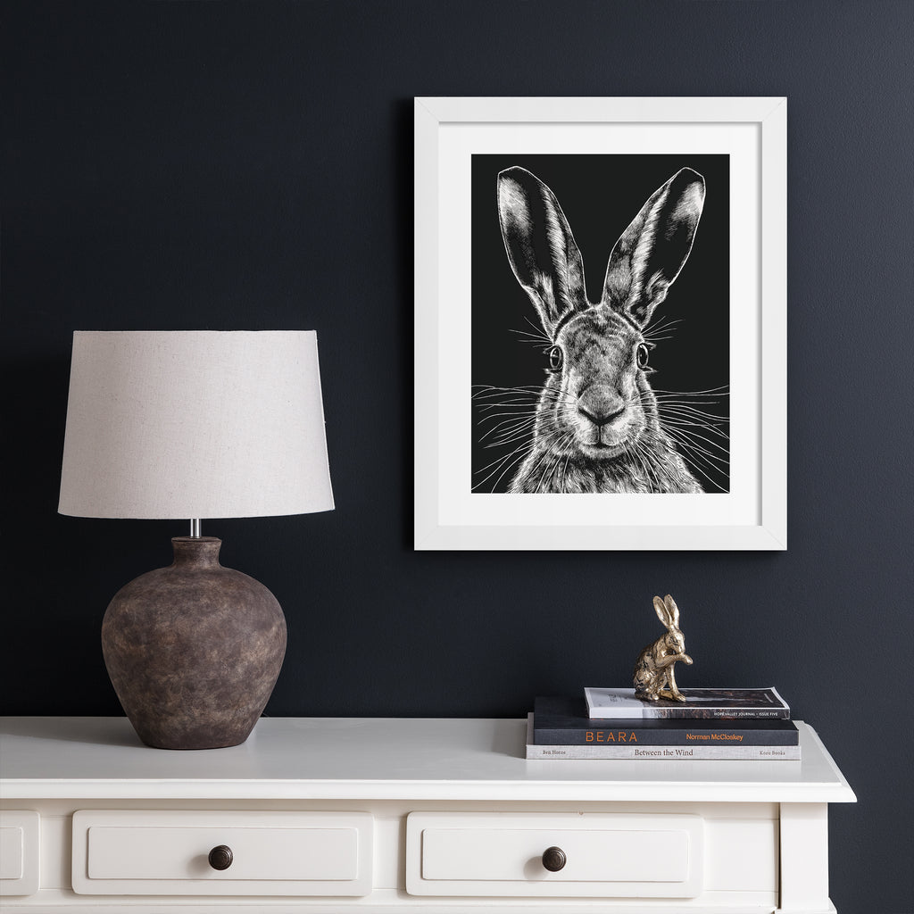 Striking art print featuring a detailed illustration of a wild hare, in black and white. Art print is hung up on a dark blue wall.