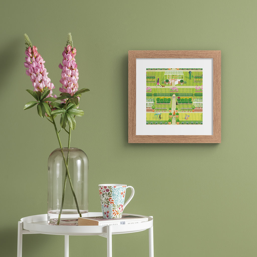 Vibrant art print featuring a symmetrical green garden, filled with a greenhouse, animals, gardeners and blooming botanicals. Art print is hung up on a sage green wall.