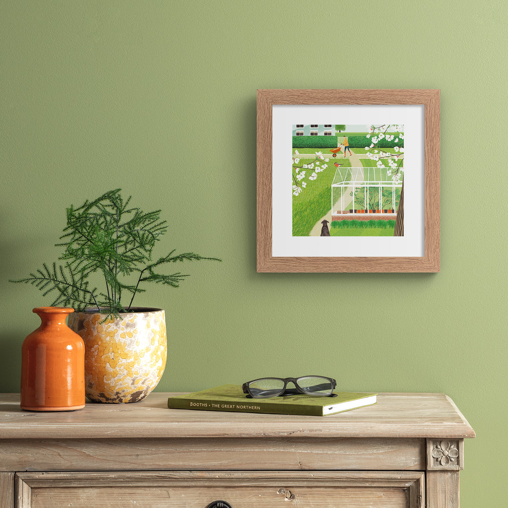 Beautiful art print featuring two characters in a vibrant green garden.  Art print is hung up on a sage green wall.