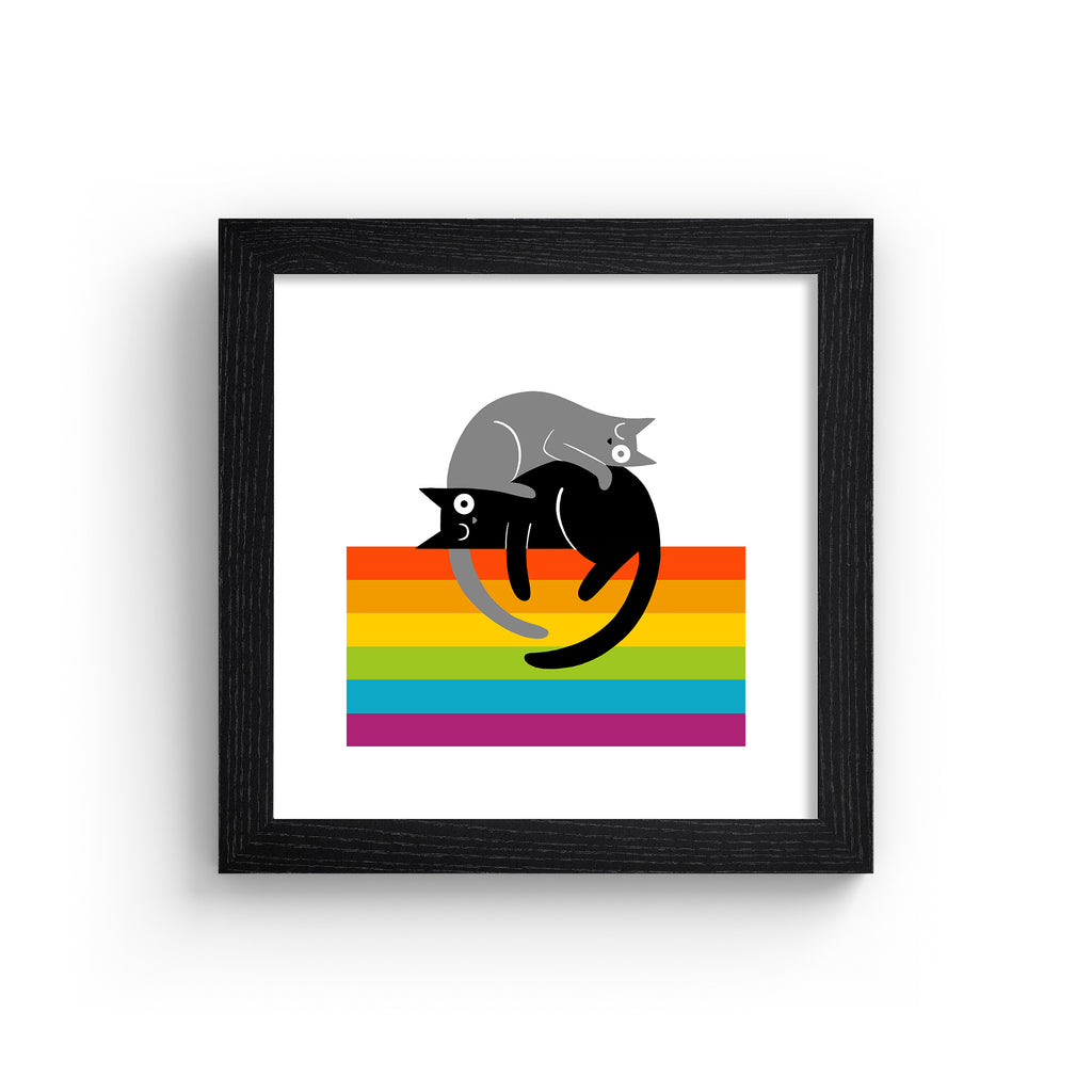 Art print of two kitties lying on top of a rainbow colours. Art print is in a black frame.